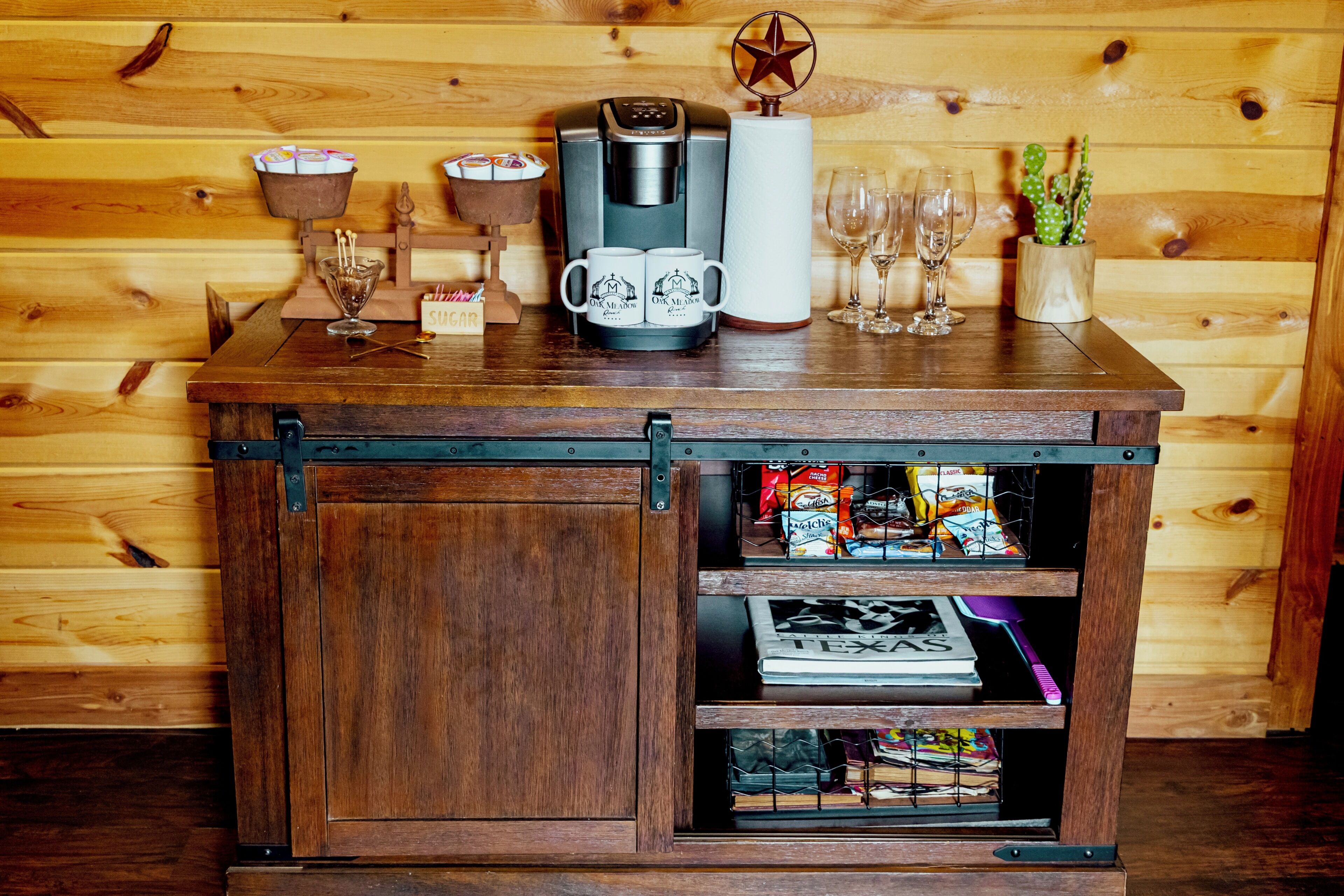 A wooden cabinet with a coffee maker, mugs, and a cactus.