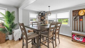 Un comedor con una mesa y sillas de madera, una estantería y una ventana con persianas.