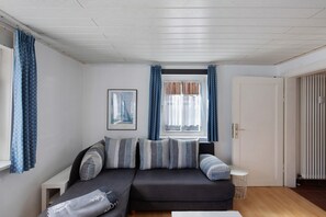 A living room with a sofa, a small table, a window with curtains, and a door.
