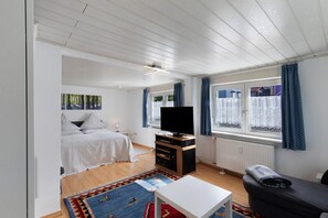 A room with a bed, a TV, a sofa, a small table, and a window with curtains.