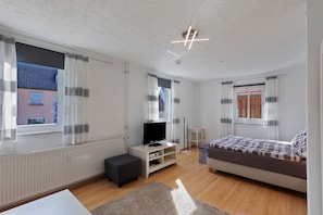 Un dormitorio moderno con cama, televisor en un mueble bajo, una mesita y un radiador.