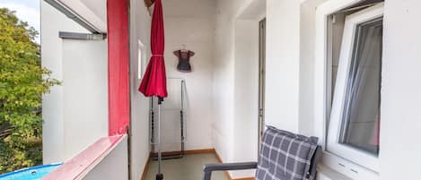 A small balcony with a chair, a red umbrella, a floor lamp, and a window.