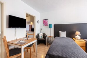 A hotel room with a bed, a desk, a chair, a TV, a clock, a picture, and a lamp.