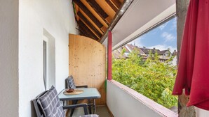 En balkong med ett bord och två stolar, en vägg av trä och utsikt över hus och grönska.