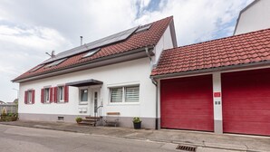 Ett tvåvåningshus med en röd garageport, en liten veranda med en bänk och en solpanel på taket.