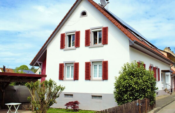 A two-story house with red shutters, a satellite dish, and a small garden.