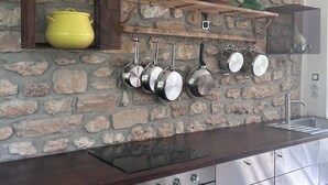 Una cocina con pared de piedra, estantes de madera, ollas colgantes y horno empotrado.