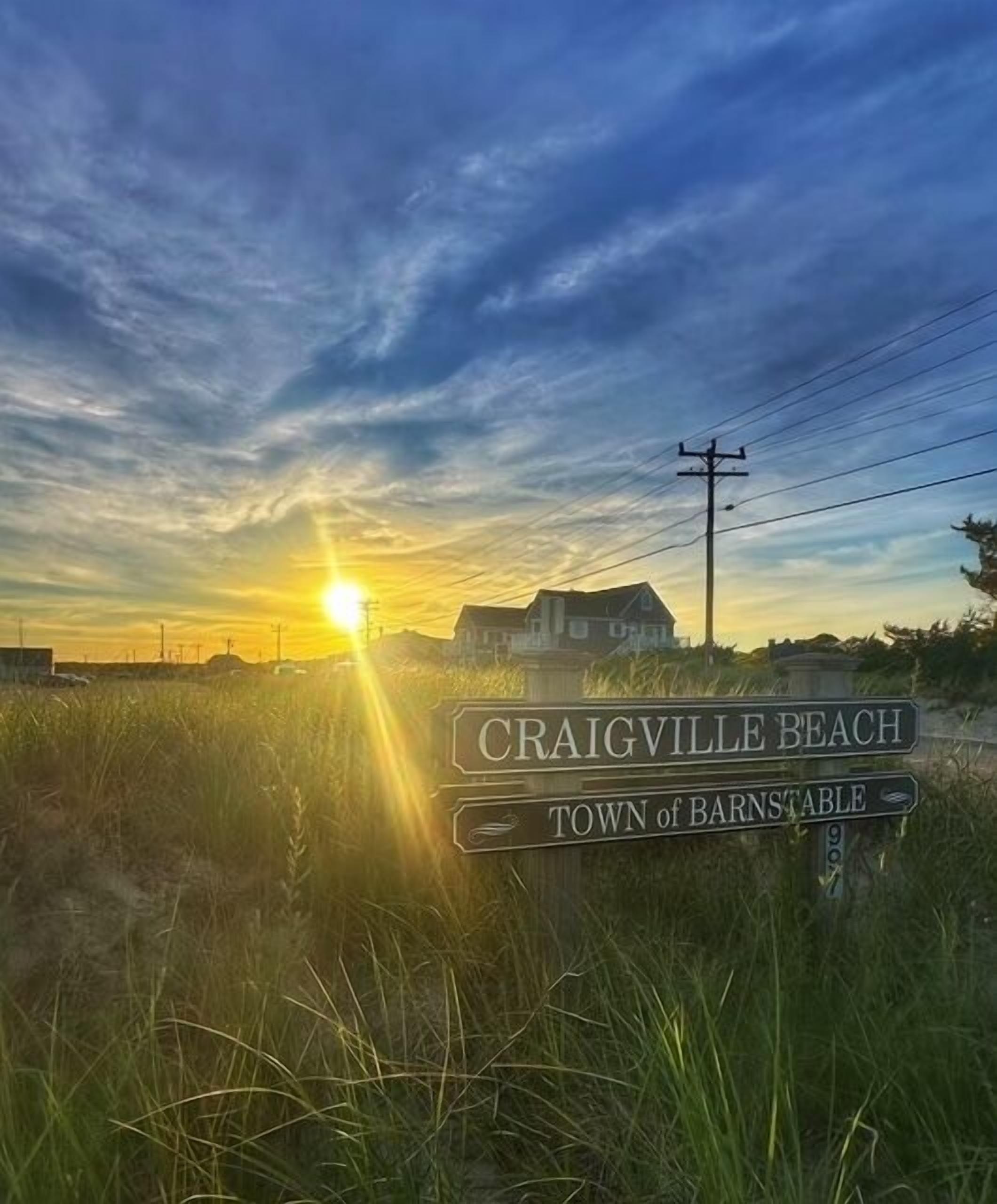 A sign for Craigville Beach, Town of Barnstable, with a sunset in the background.