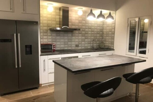 A modern kitchen with a large island, stainless steel appliances, and pendant lighting.
