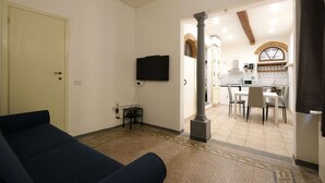 A living room with a sofa, a TV mounted on the wall, and a kitchen area visible through an open doorway. - Wine Apartments Florence Sagrantino (Firenze)