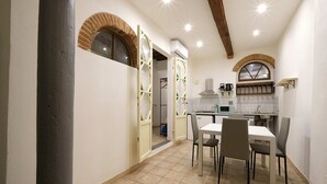 A compact kitchen with a dining area, featuring a tiled floor, a white table, and chairs. - Wine Apartments Florence Sagrantino (Firenze)