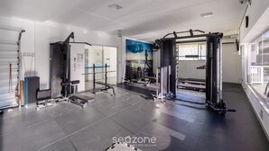 Une salle de sport équipée de divers appareils d’exercice, un mur orné d’une fresque bleue et blanche, et une fenêtre laissant entrer la lumière naturelle.