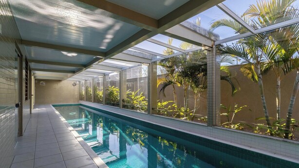 Une piscine dotée d’une enceinte en verre, entourée de palmiers et dont le sol est recouvert de carreaux.