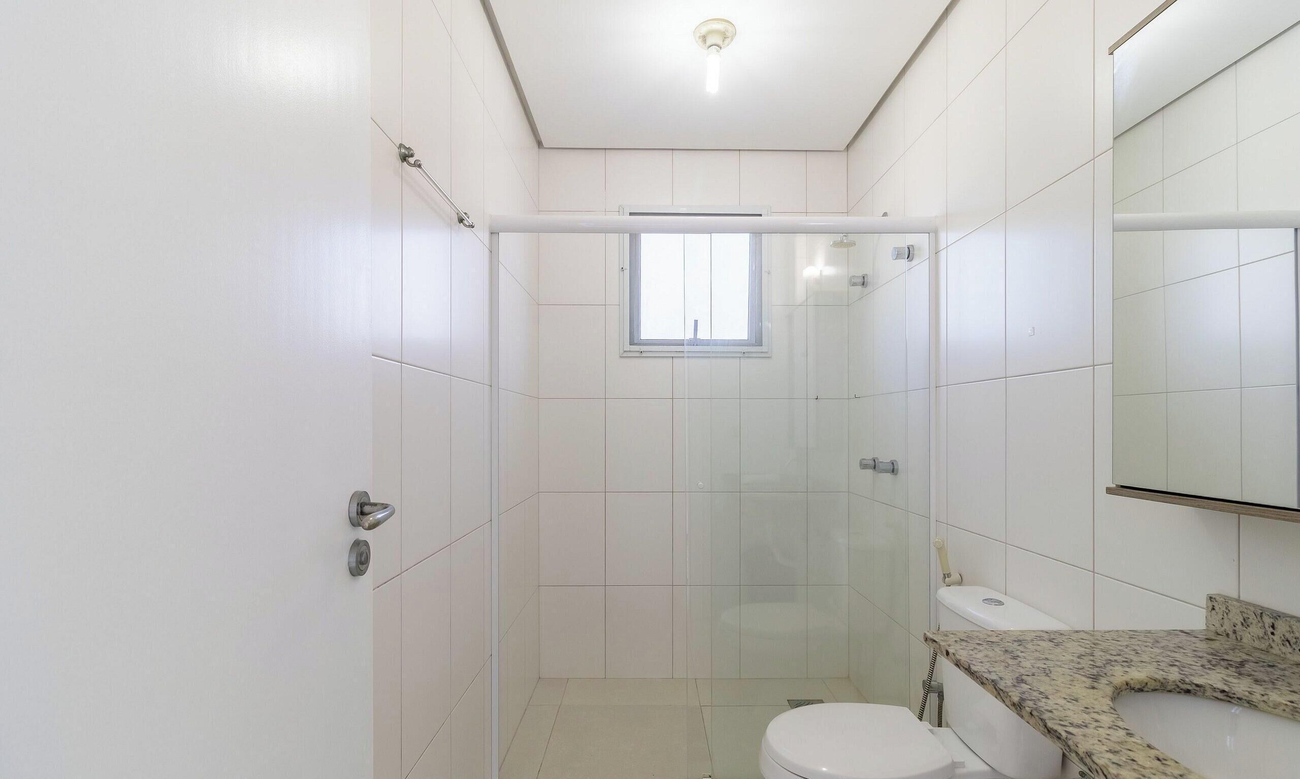 Een kleine, moderne badkamer met witte tegels, een glazen douchecabine, een toilet en een granieten aanrechtblad.