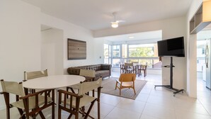Un vaste espace de vie comprenant une table à manger, un canapé et des fauteuils. Un téléviseur à écran plat est fixé au mur.