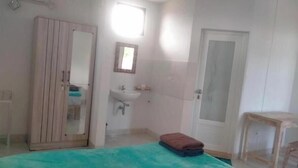 Un dormitorio con cama, armario, baño con lavabo y espejo, y una puerta.