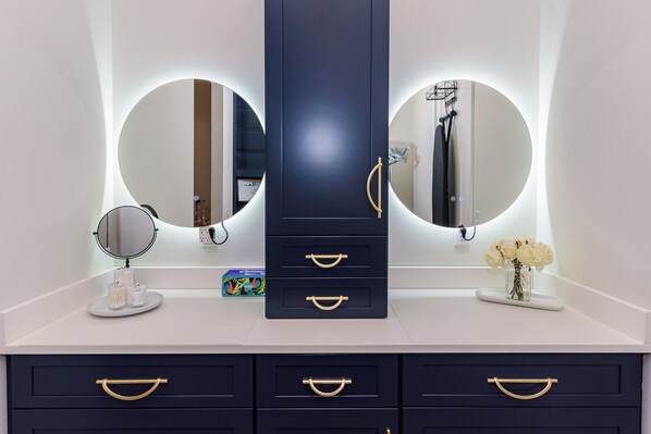 A bathroom vanity with two large mirrors, a central cabinet with drawers, and a small vase with flowers on the countertop.
