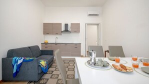 Una cocina moderna con armarios empotrados, una mesa de comedor dispuesta para el desayuno y un sofá gris con una manta.
