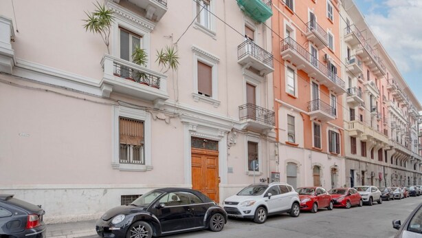 Una hilera de edificios de varios pisos con balcones, autos estacionados y un cielo despejado.
