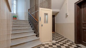 Una escalera con piso a cuadros, una puerta con un pequeño ventanal y una planta en maceta.