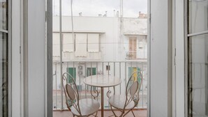 Un balcón con mesa y sillas, vistas a edificios y una valla de malla.