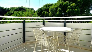 Ein Balkon mit rundem Tisch und vier Stühlen, umgeben von einer weißen Brüstung und Grünpflanzen im Hintergrund.