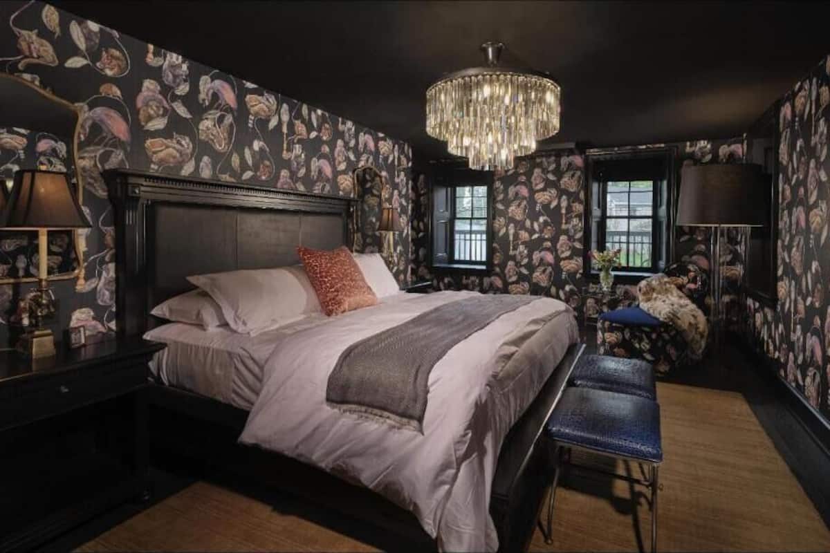 A bedroom with a large bed, a chandelier, a desk, and a bench.