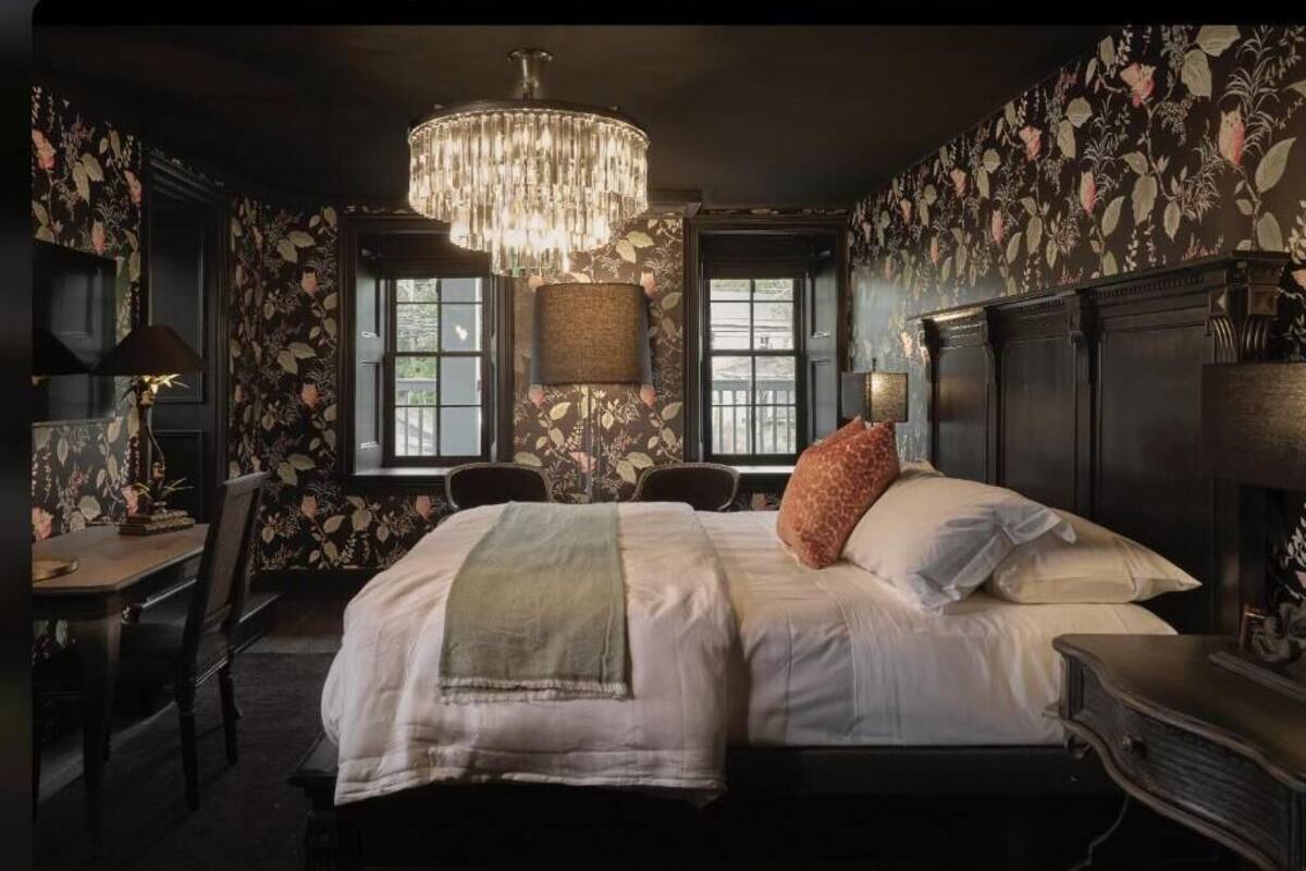 A bedroom with a large bed, two bedside tables, a chandelier, and floral wallpaper.