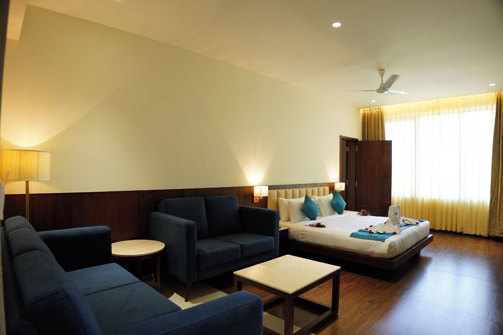 A hotel room with a bed, two sofas, a small table, and a ceiling fan.
