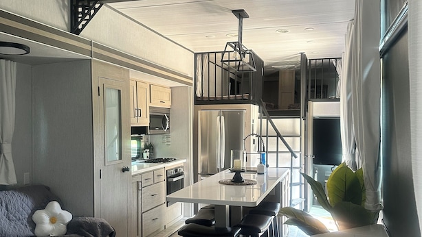 A compact kitchen with a central island, a ceiling fan, and a staircase leading to an upper level.