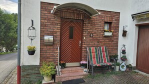 Ein Backsteinhaus mit Holztür, einer Bank davor und Blumentöpfen.