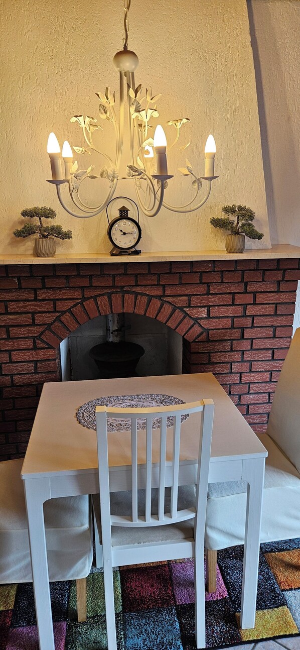 A dining area with a table, chairs, a chandelier, a clock, and a brick fireplace.