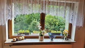 Ein Fenster mit Spitzenvorhängen, Blick ins Grüne und ein kleiner Tisch mit Dekoration.
