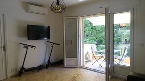 A modern living room with a large sliding glass door leading to an outdoor area, a flat-screen TV mounted on the wall, and two electric scooters. - Enchanting apartment with AC in Cannes (Cannes)