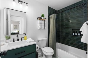 A modern bathroom with a white sink, black faucet, green cabinets, a white toilet, and a shower with green tiles. - Premier Access to Zilker Park & South Congress (Austin)