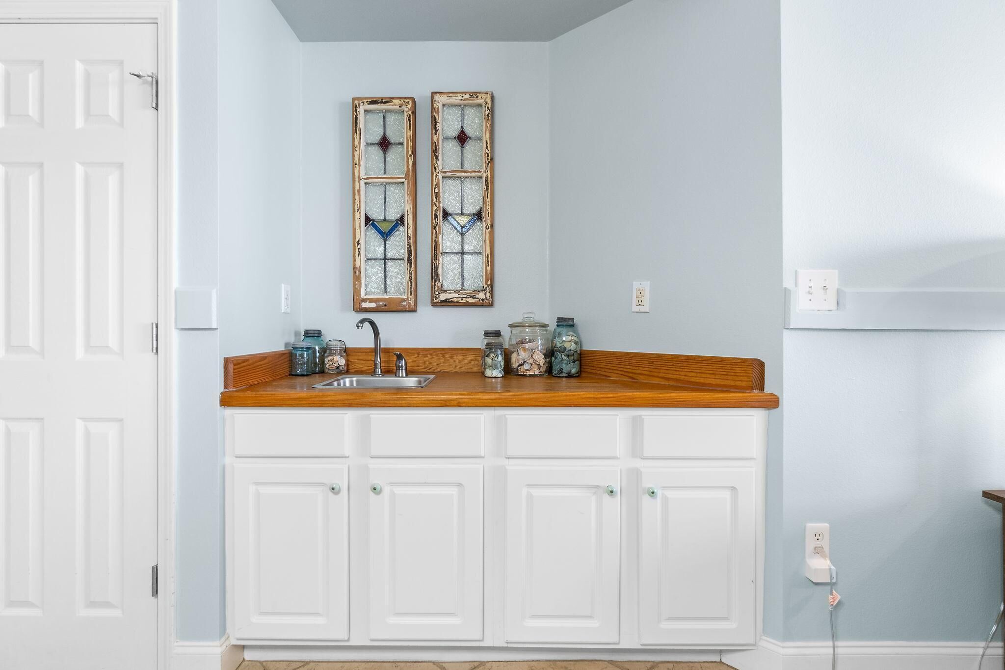 A kitchen with white cabinets, a wooden countertop, a sink, and two decorative stained glass windows.