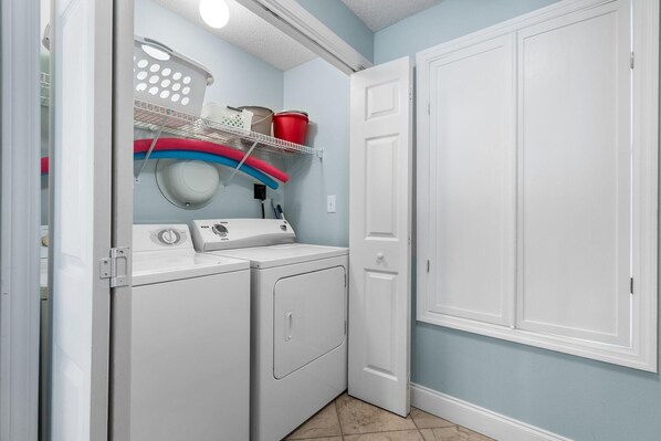 A laundry room with a washing machine, dryer, and shelves with baskets and containers.