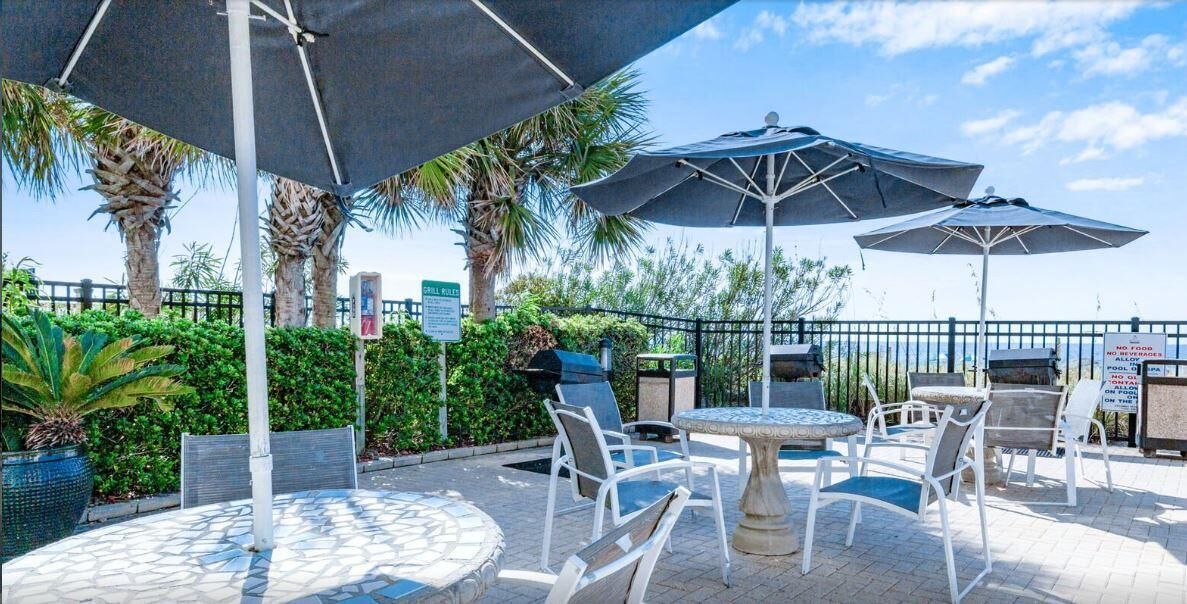 An outdoor patio with round tables and chairs, umbrellas, and a grill area.
