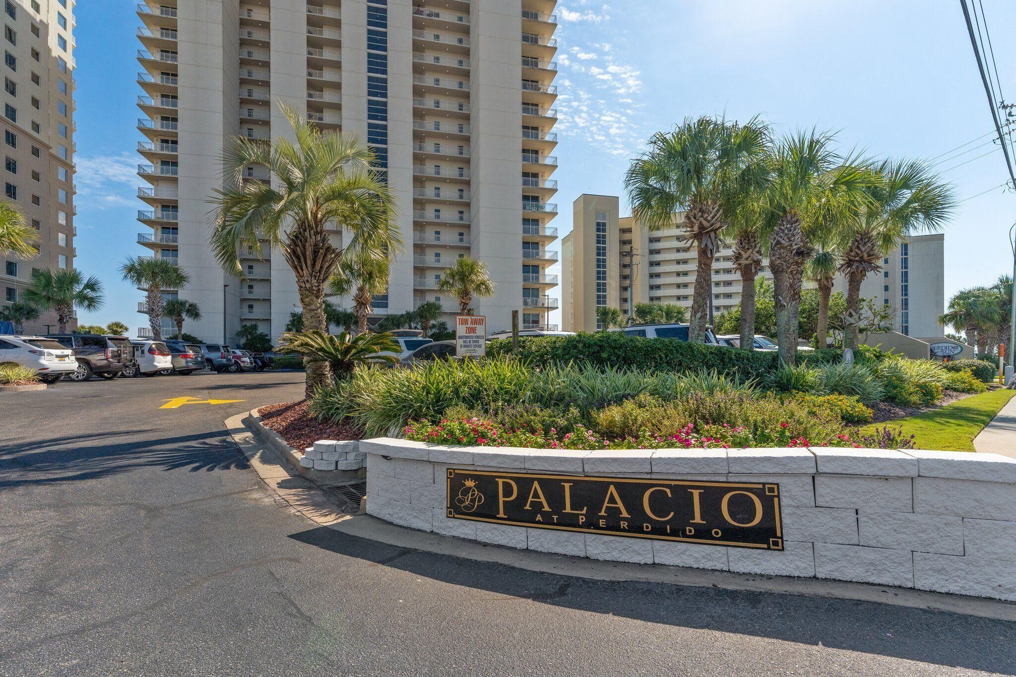 A sign for "Palacio at Perdido" with a landscaped area in front, palm trees, and high-rise buildings in the background.