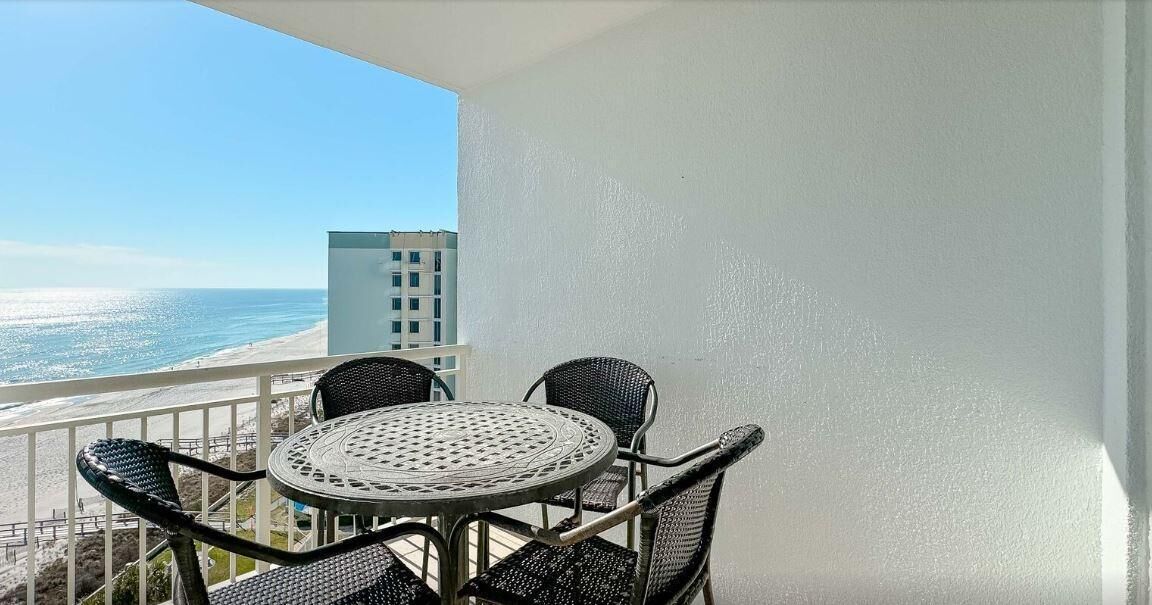 A balcony with a round table and four chairs, overlooking a beach and ocean.