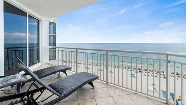 A balcony with two wicker lounge chairs, a table, and a view of the beach and ocean. - Palacio 802 (Pensacola)