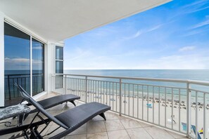 A balcony with two wicker lounge chairs, a table, and a view of the beach and ocean. - Palacio 802 (Pensacola)