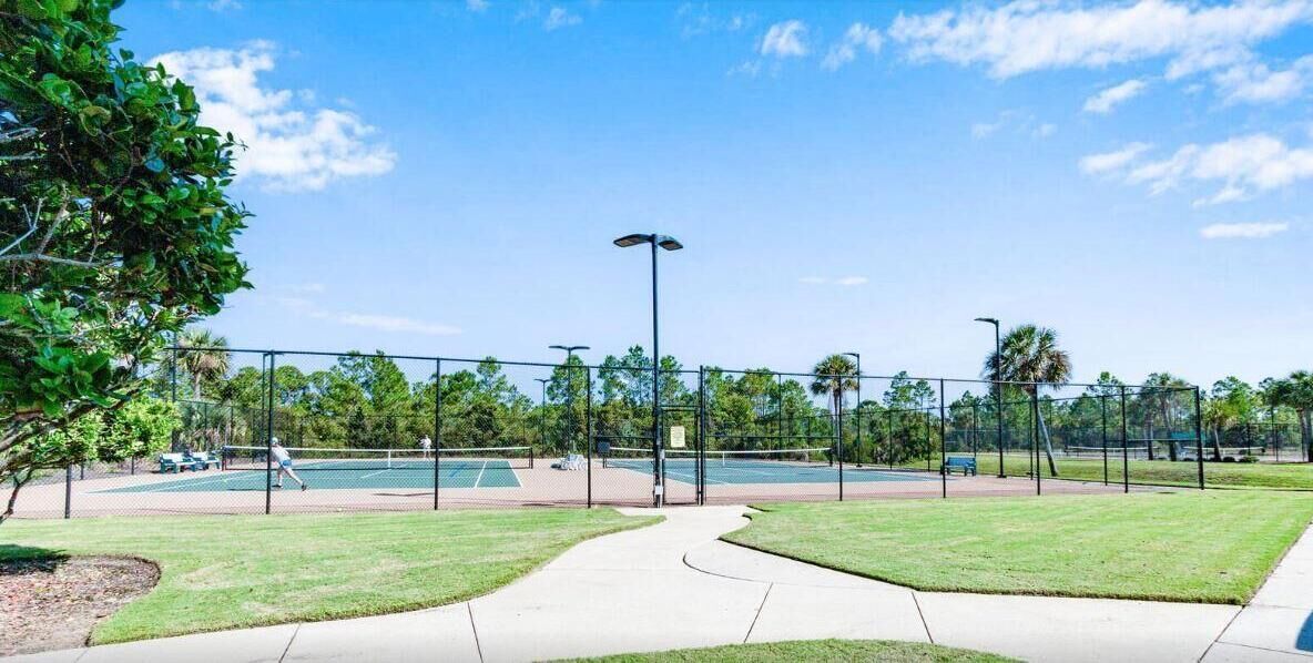 Un campo da tennis con una recinzione, un vialetto e alberi sullo sfondo.
