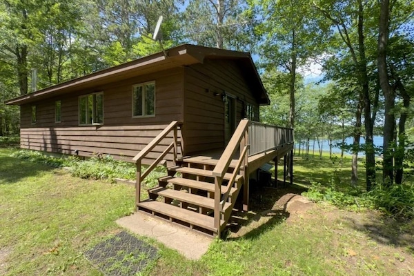 This cabin showcases a wooden exterior with a spacious deck that leads into a lush yard, perfect for outdoor activities.