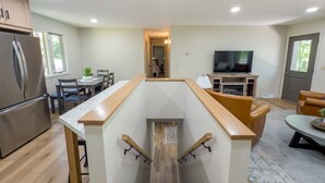 Cozinha moderna com geladeira embutida, área de refeições com mesa e cadeiras, televisão e escada com corrimão de madeira.