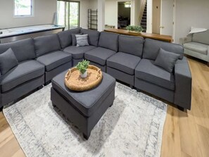 A modern living room with a grey sectional sofa, a small ottoman with a plant, and a white patterned rug.