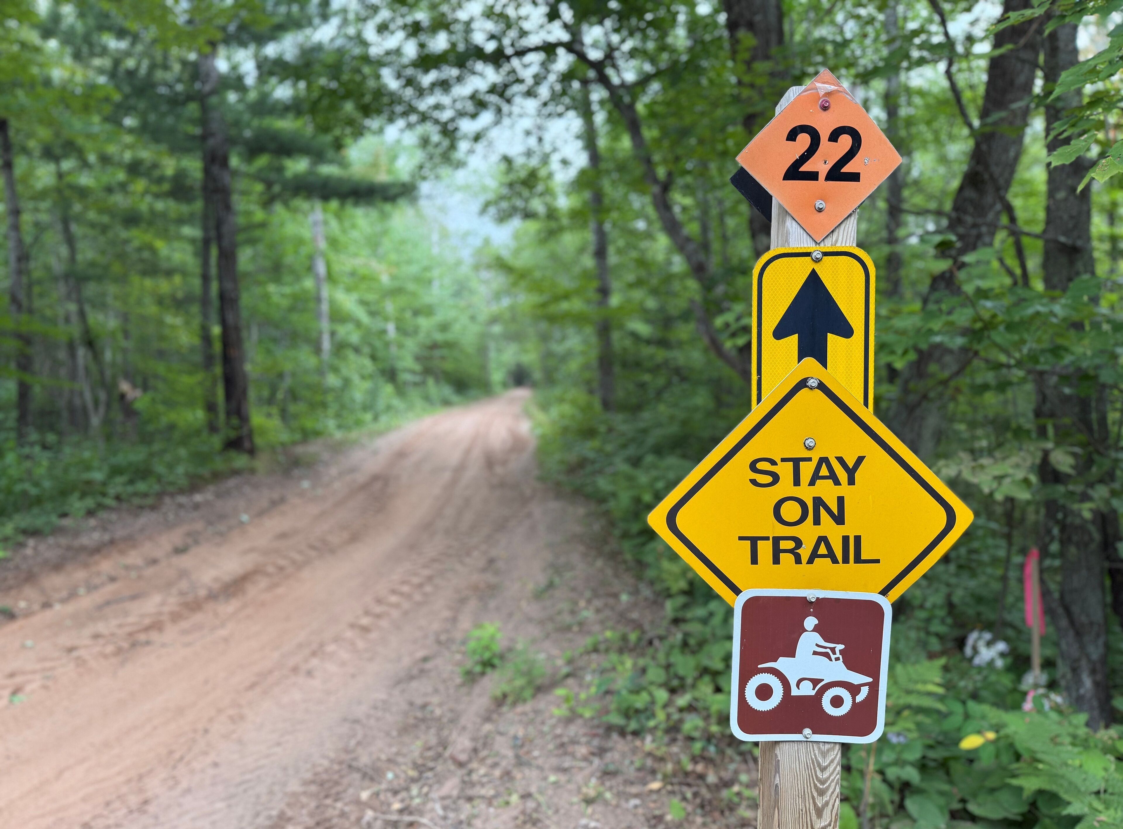 A trail sign with a number 22, a 'Stay on Trail' sign, and a symbol for a dirt bike trail.