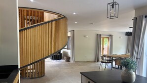 A modern kitchen with a curved wooden staircase, a dining area with a table and chairs, and a view of the outdoors through a door. - Lime Tree House - Sleeps 12 - Hot Tub (Sudbury)