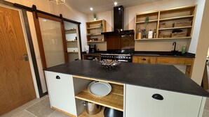 A modern kitchen with a central island, wooden cabinets, and a built-in stove. - Lime Tree House - Sleeps 12 - Hot Tub (Sudbury)