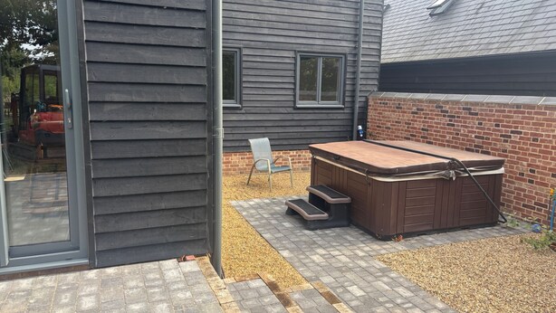 A modern house with a patio area, including a hot tub, a chair, and a small table. - Lime Tree House - Sleeps 12 - Hot Tub (Sudbury)